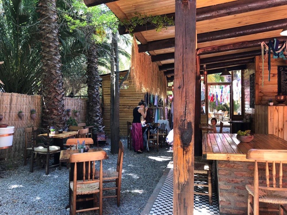 Terraza de la pastelería entre palmeras, con mesas y sillas de madera bajo pérgola