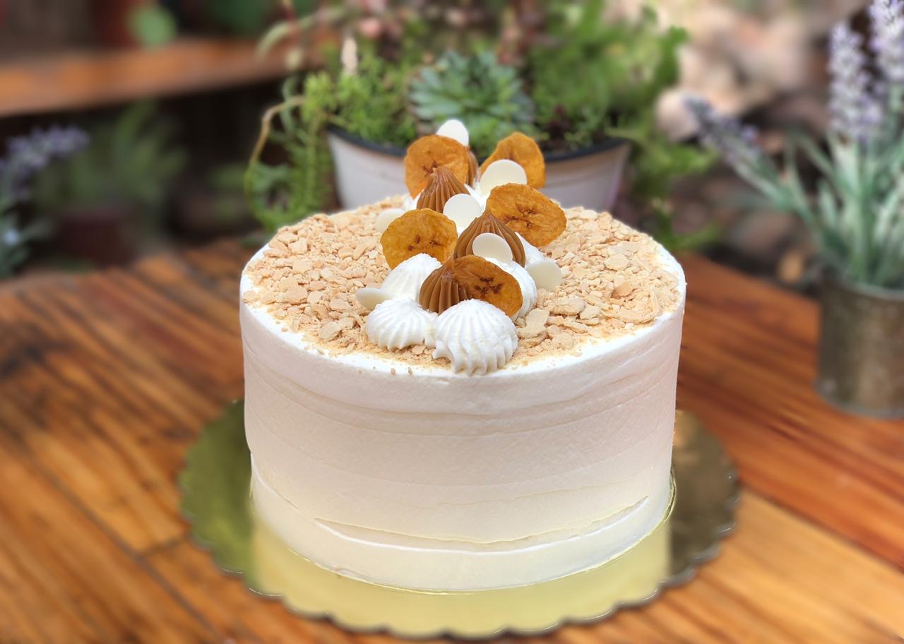 Torta de crema recién decorada con plátano deshidratado y manjar, sobre una mesa de madera de la pastelería